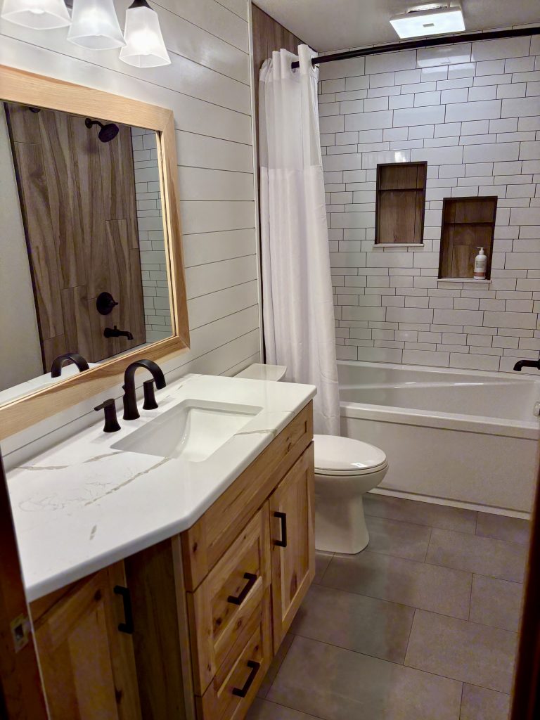 White ceramic subway tile installed in random offset pattern with wood-look porcelain sidewalls in a custom bathroom renovation in Northwest Ohio.