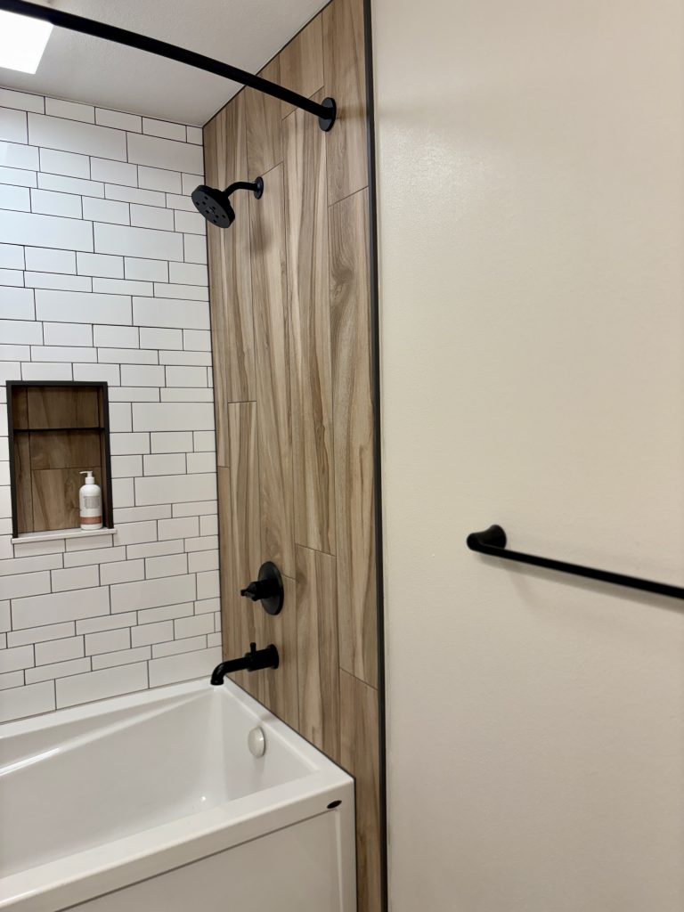 Deep soaking tub with white subway tile surround and wood-look porcelain tile sidewalls in a hallway bathroom renovation near Toledo, Ohio.