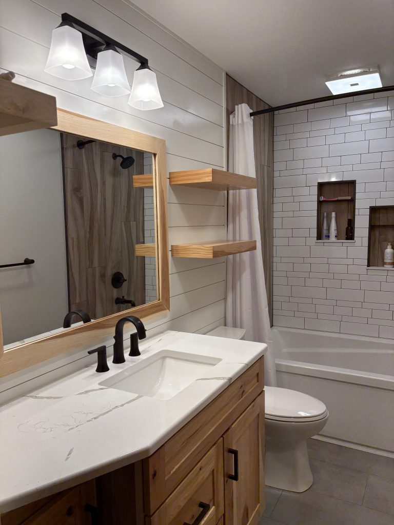Bright hallway bathroom remodel with porcelain tile flooring, shiplap accent wall, and matte black fixtures by Kleeberger Contracting Services.