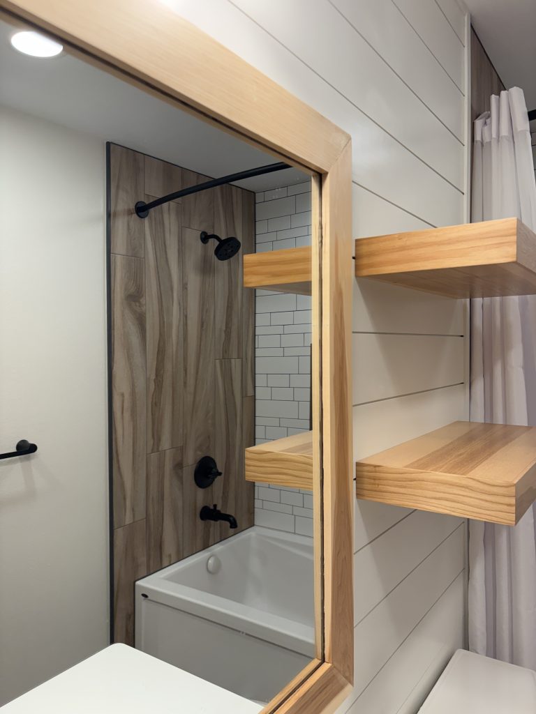 Custom maple mirror and floating shelves above a natural wood vanity in a modern rustic bathroom remodel in Northwest Ohio.